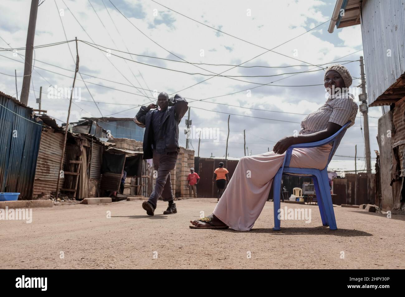 Une femme est assise sur une chaise monobloc près des rues des bidonvilles de Kibera. Banque D'Images