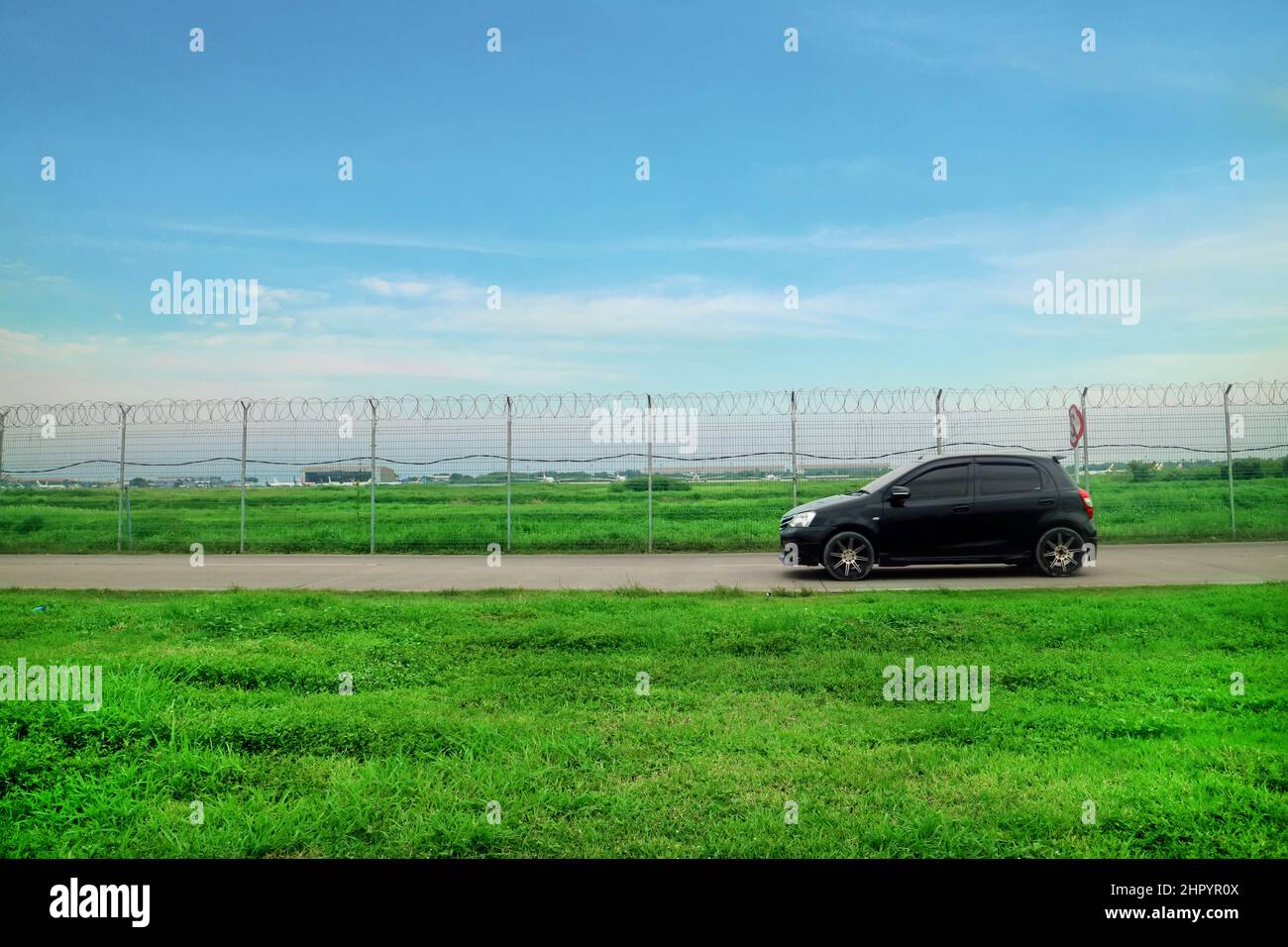 Route à l'extérieur de l'aéroport bordée d'un fil de Fence avec herbe verte et voiture noire Banque D'Images