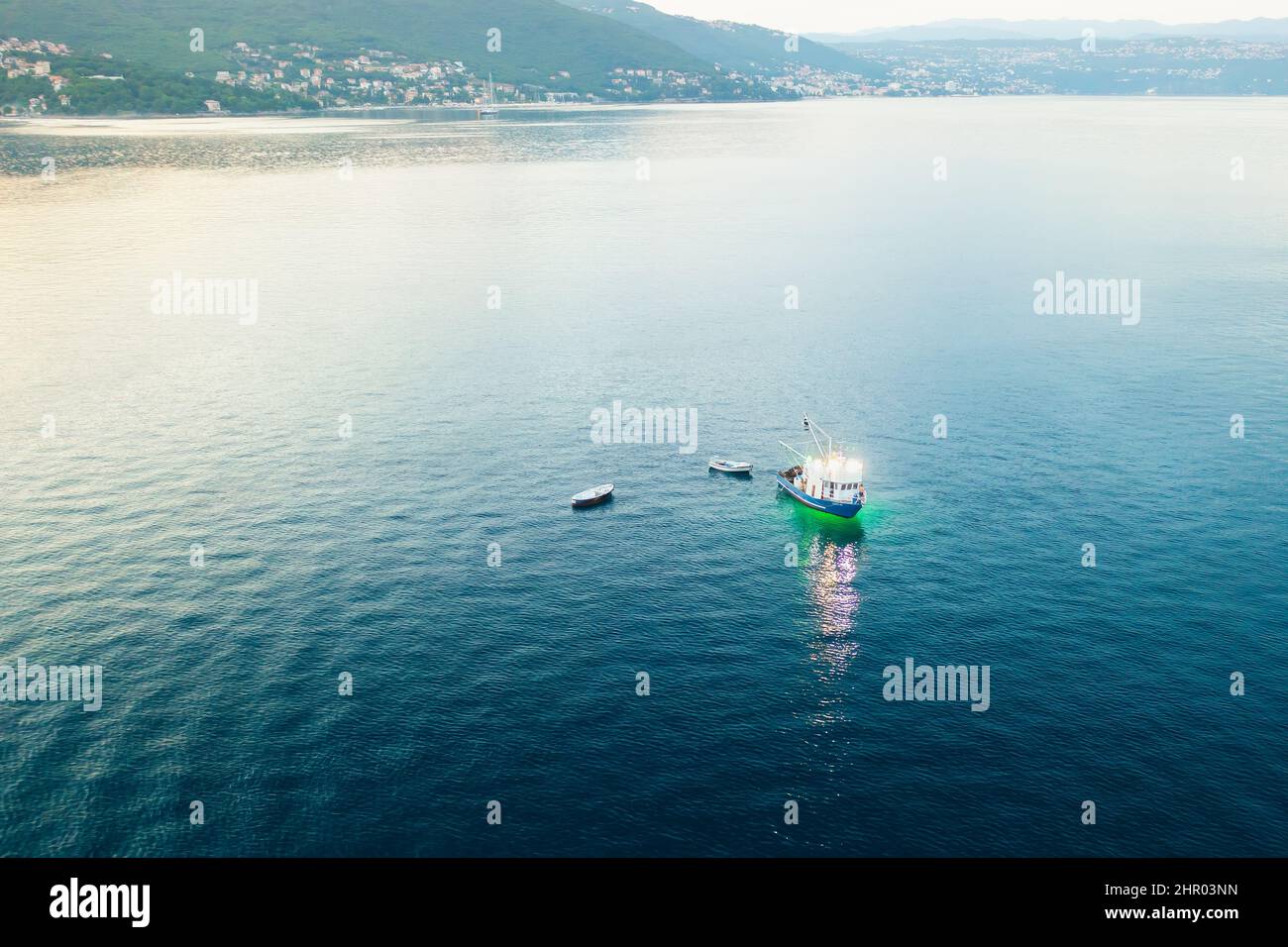 Pêche en bateau éclairant les eaux de la mer Adriatique avec lampe de poche. Crépuscule sur mer et péninsule couverte de forêts et de bâtiments. Vue aérienne Banque D'Images