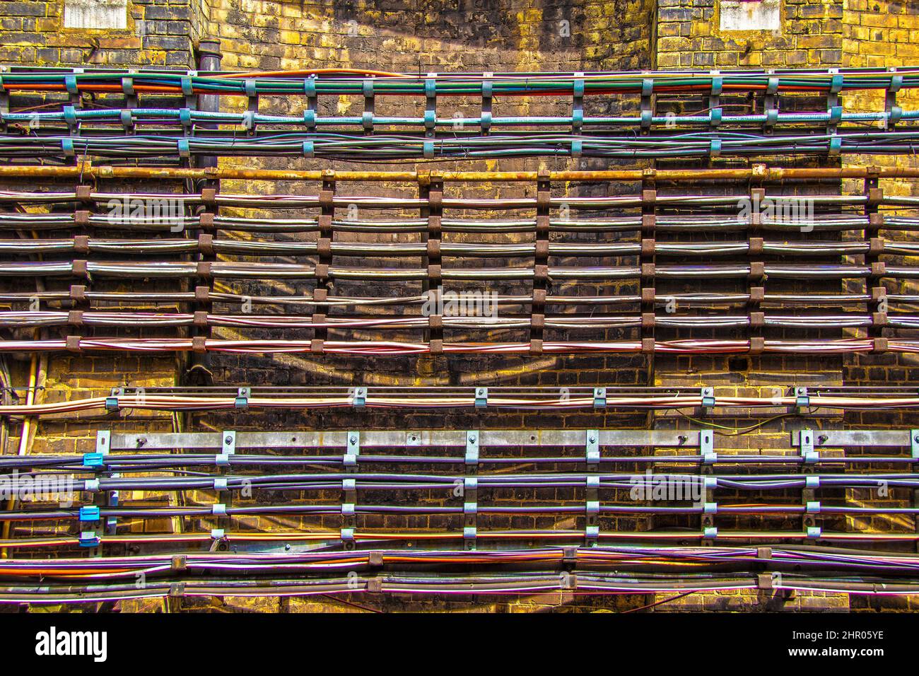 Rangées de fils et de tuyaux sur les racks fixés au mur de briques grungy dans le chemin de fer souterrain Banque D'Images