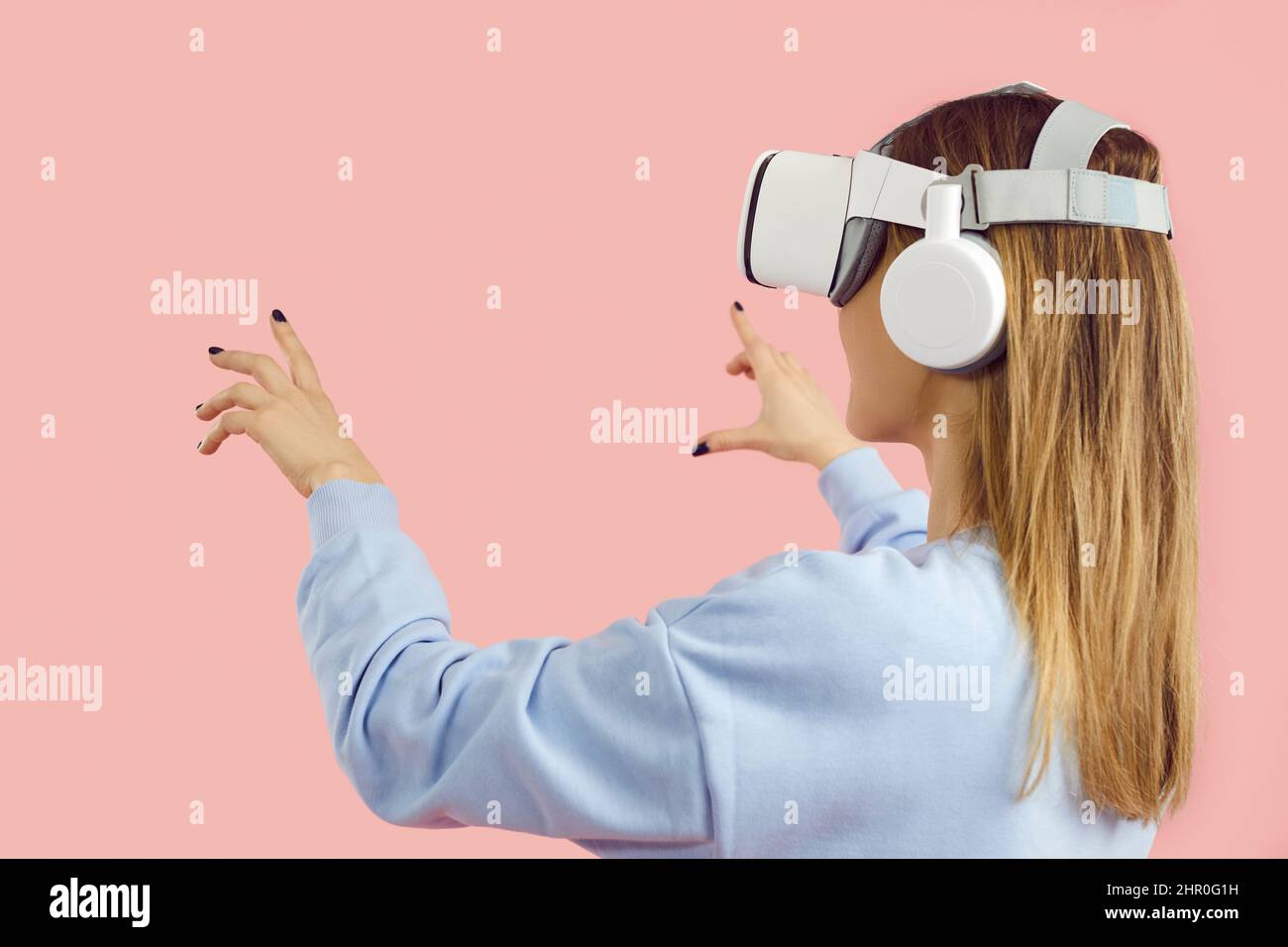 Fille dans un casque innovant jouant à des jeux vidéo, faisant l'expérience de VR, touchant des objets virtuels Banque D'Images