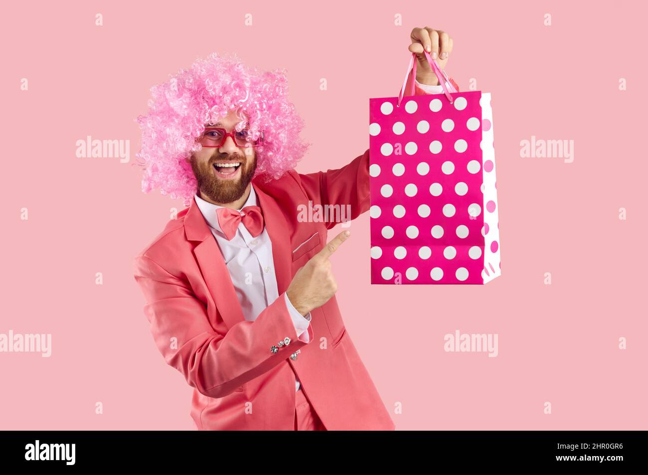 Clown drôle en costume rose, perruque et verres montrant le sac de papier et sourire Banque D'Images