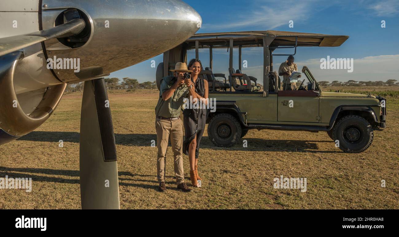 Un jeune et attrayant couple tanzanien portant des vêtements tropicaux, en safari dans une réserve de gibier, à côté de leur avion privé affrété. Banque D'Images