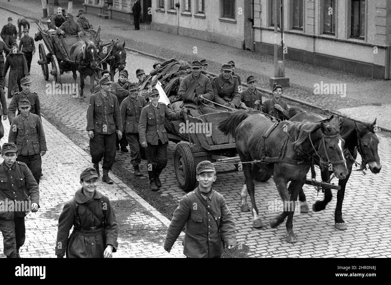 Allemagne Seconde Guerre mondiale 1945. Soldats de l'armée allemande la plupart d'entre eux très jeunes souriant comme ils retournent à la maison défait avec un drapeau blanc de la reddition sur leur cheval et chariot. Des drapeaux blancs peuvent également être vus drapés de certains des buidlings. Banque D'Images