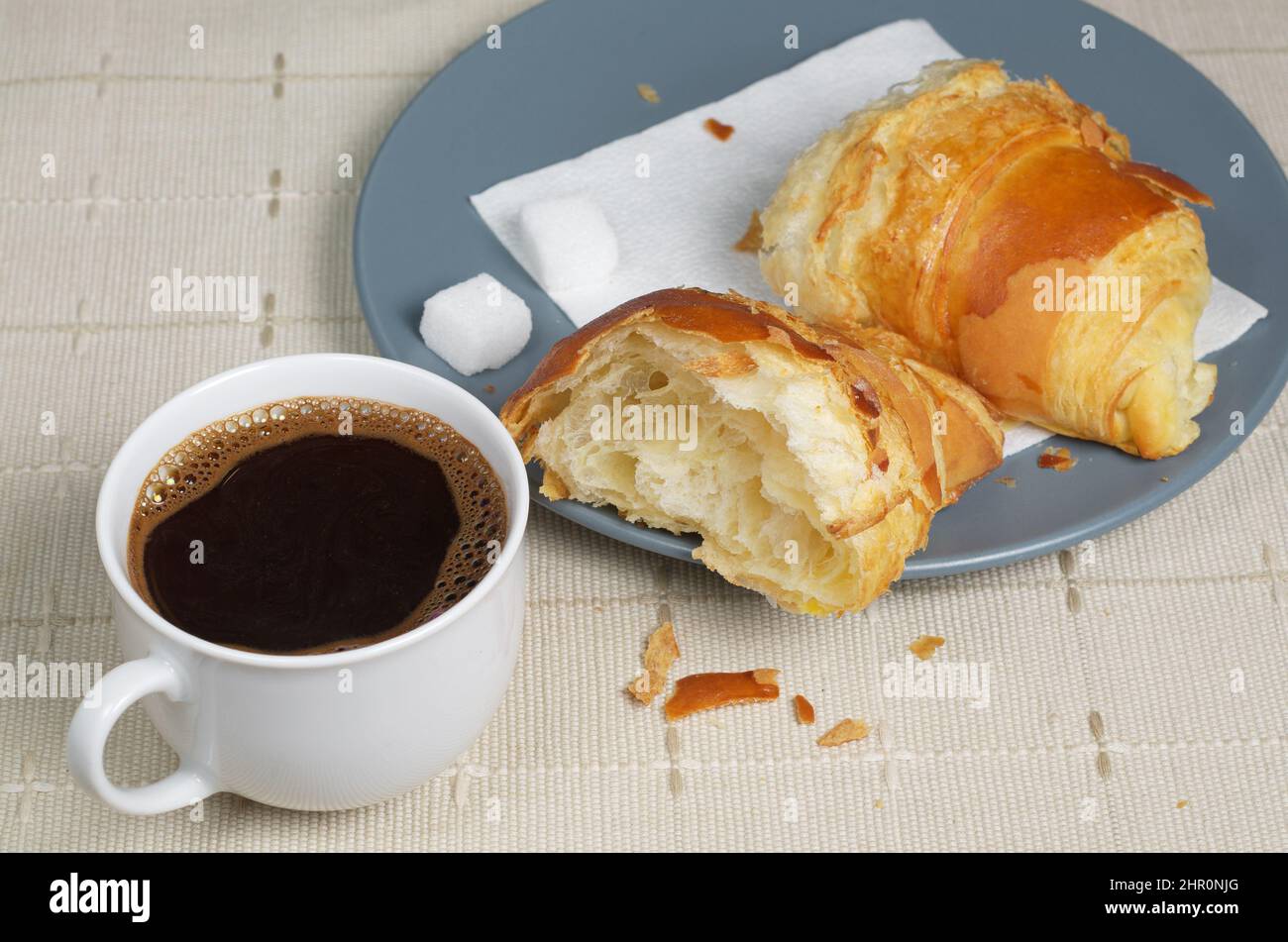 Une tasse de café et un demi croissant sur une assiette grise sur une table avec une nappe. Thème du petit déjeuner ou de la pause Banque D'Images