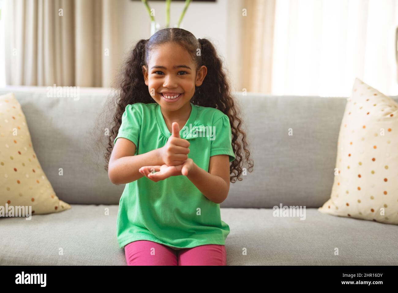 Portrait d'une fille muette multiraciale souriante parlant à la main en langage des signes assis sur un canapé à la maison Banque D'Images