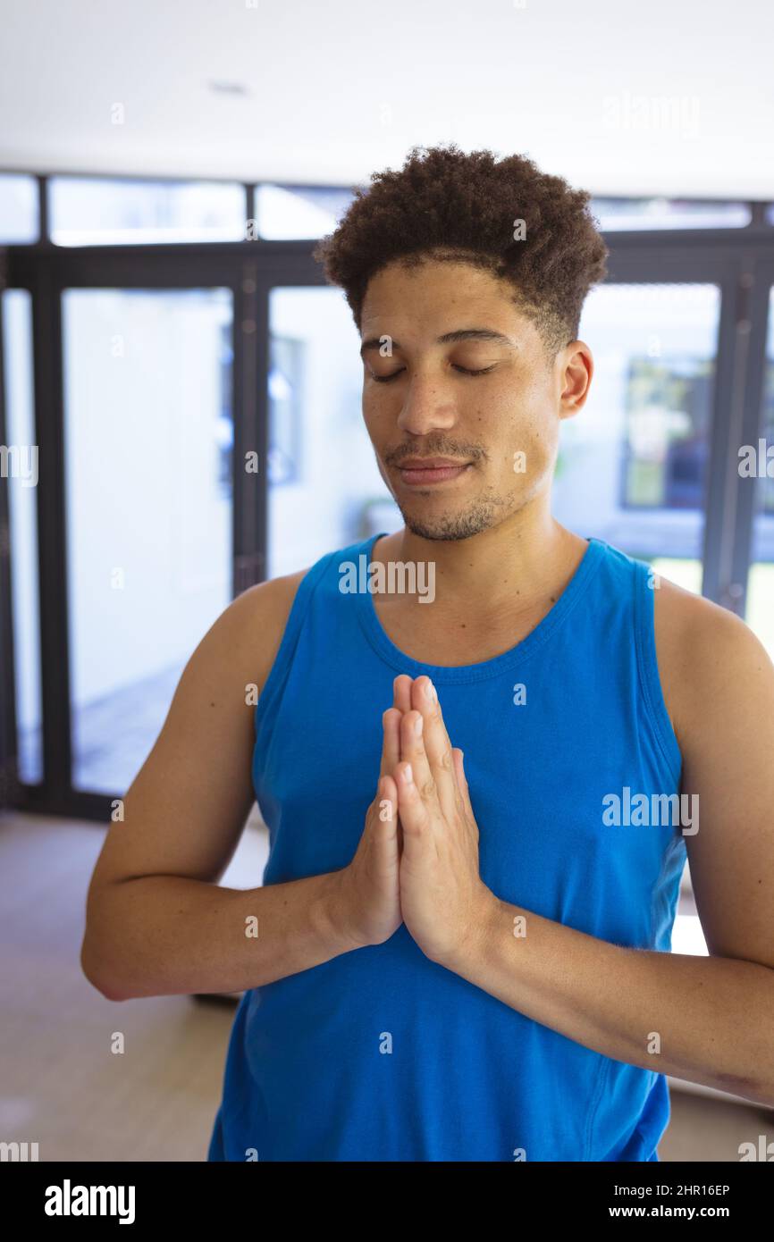 Jeune homme multiracial pratiquant le yoga en se tenant debout avec les mains jointes à la maison Banque D'Images