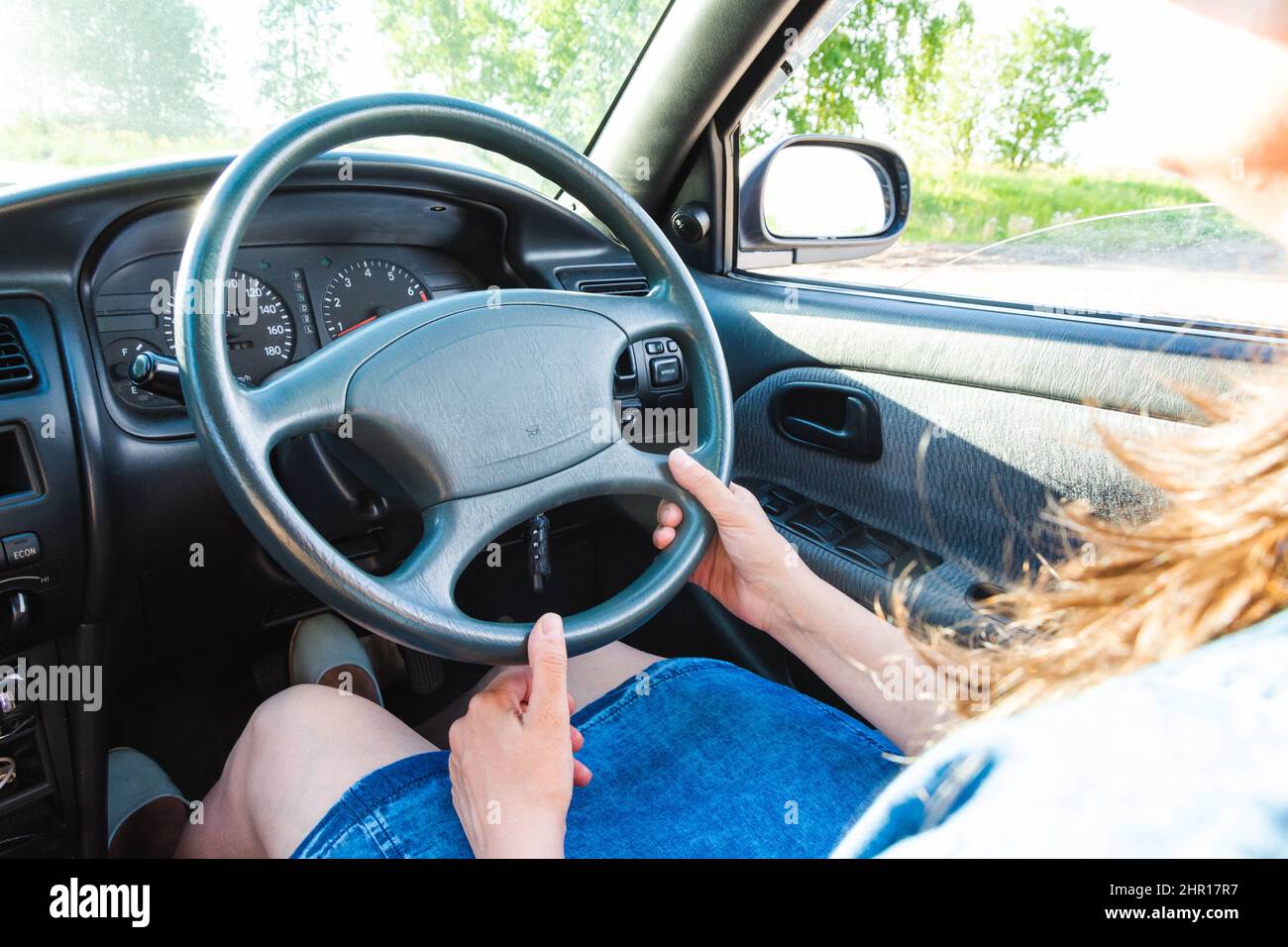 Une brunette en Jean conduit une vieille voiture japonaise avec une conduite à droite. Banque D'Images
