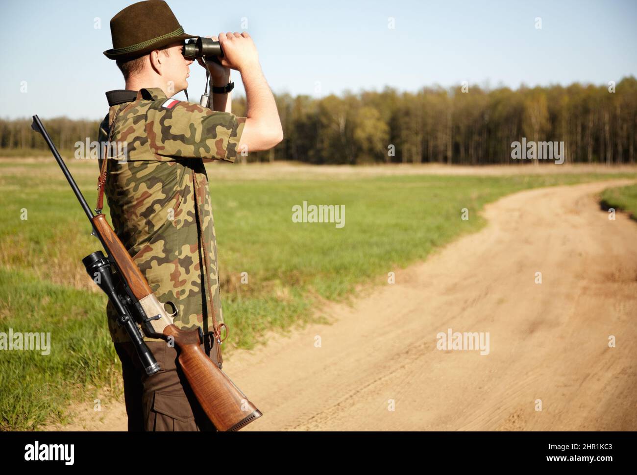 Sur le coup d'œil. Un garde-manger de jeu avec son fusil regardant à travers ses jumelles à l'extérieur avec copyspace. Banque D'Images