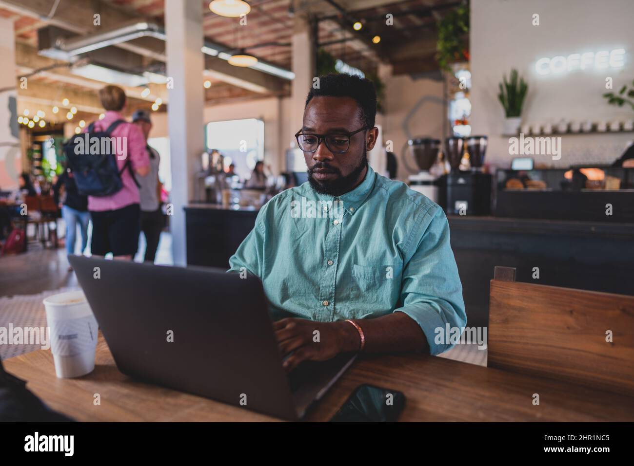 jeune homme noir à l'aspect professionnel travaillant sur un ordinateur portable dans un café avec téléphone portable et café Banque D'Images