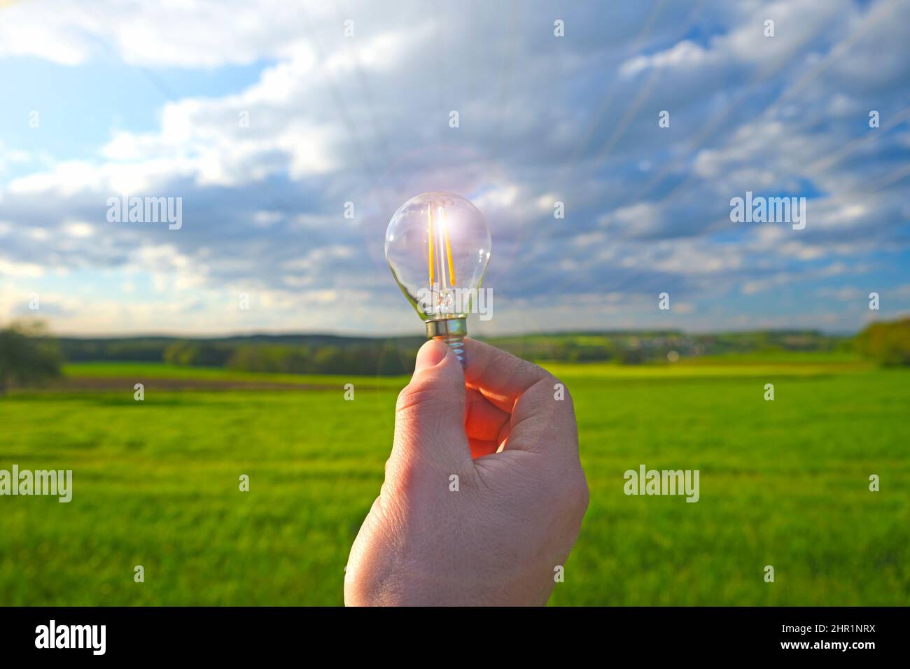 Électricité et énergie verte.ampoule à la main sur fond bleu ciel et vert champ.sources d'énergie naturelles alternatives Banque D'Images