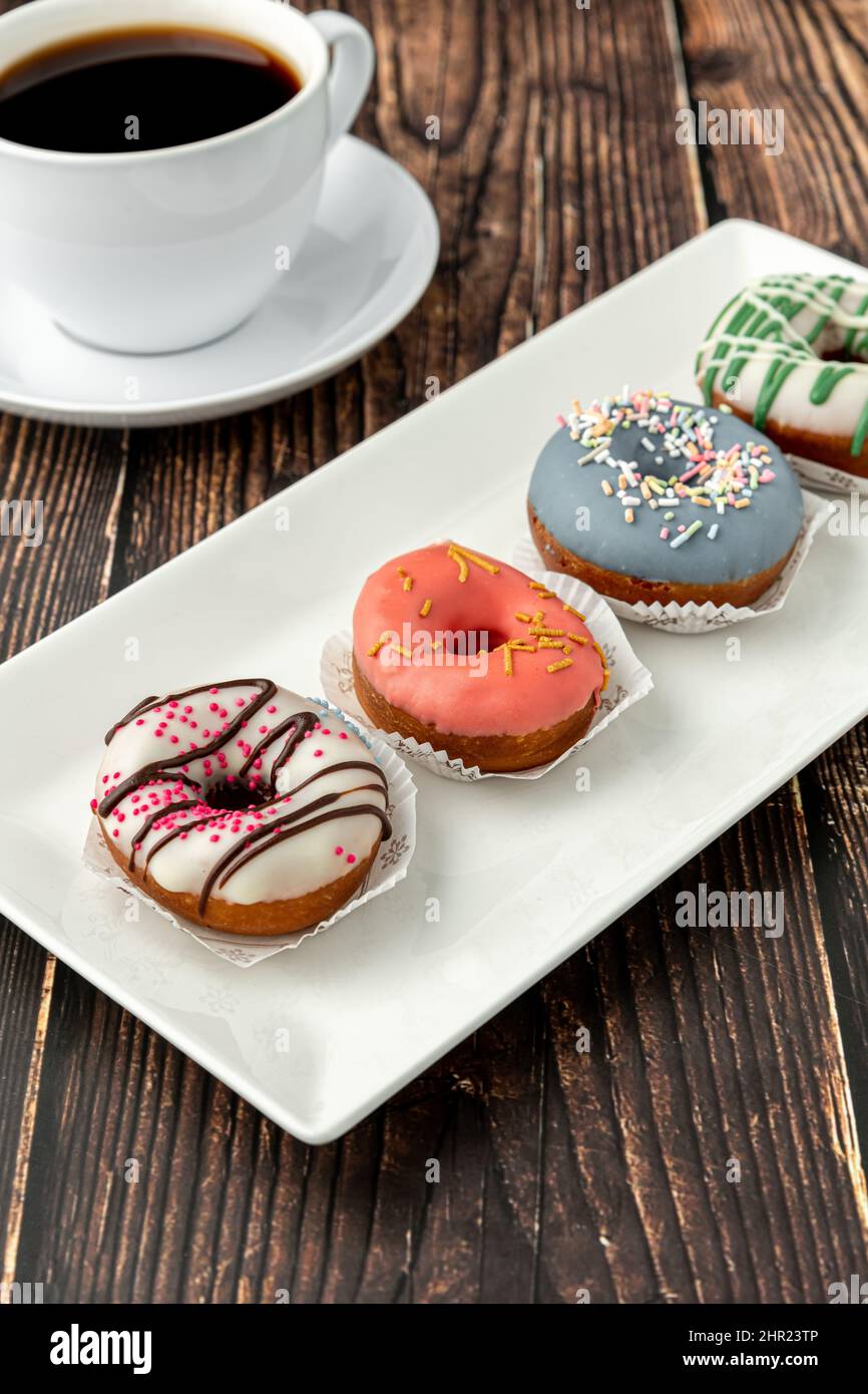 Délicieux mini beignets colorés avec café sur table en bois Banque D'Images