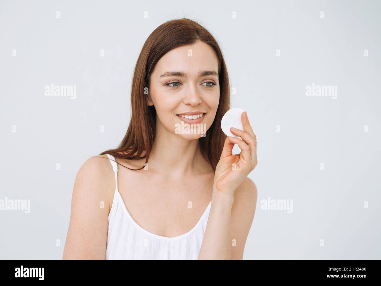 Portrait de beauté de la jeune femme souriante heureuse avec des cheveux longs foncés et propre visage de peau fraîche avec tampon de coton à la main sur fond blanc isolé Banque D'Images