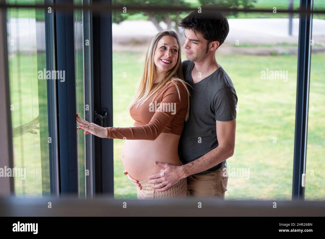 Jeune homme embrassant sa femme enceinte et regardant par la fenêtre Banque D'Images
