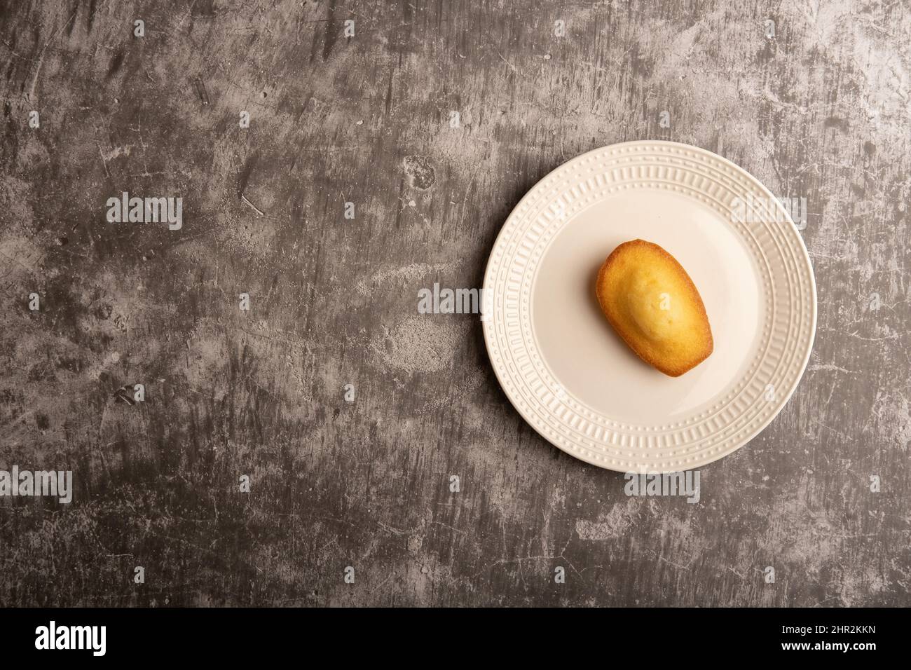 Gâteau Madeleine sur une plaque blanche contre un fond gris texturé béton plat. Banque D'Images