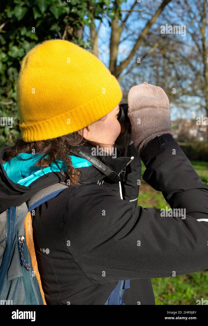 Personne avec un chapeau et des gants d'observation des oiseaux lors d'une journée d'hiver ensoleillée dans la nature Banque D'Images
