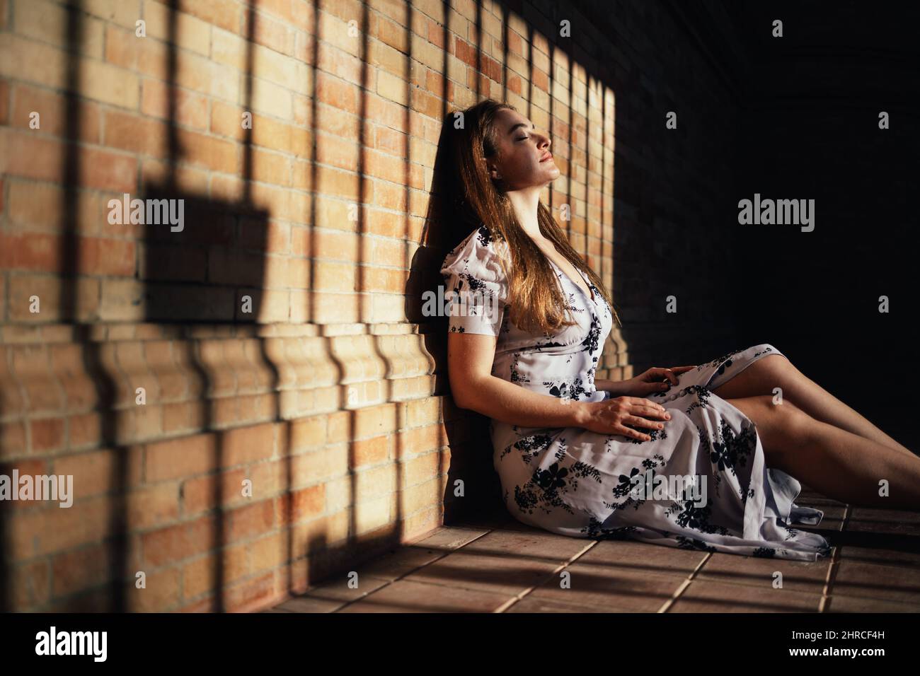 Femme caucasienne assise sur le sol appréciant la sensation de la chaleur du soleil sur son visage qui entre de l'extérieur Banque D'Images