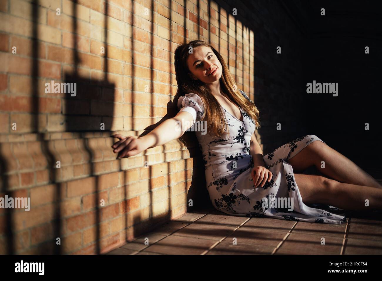 Femme caucasienne assise sur le sol, appuyée contre un mur de briques et souriant à l'appareil photo Banque D'Images