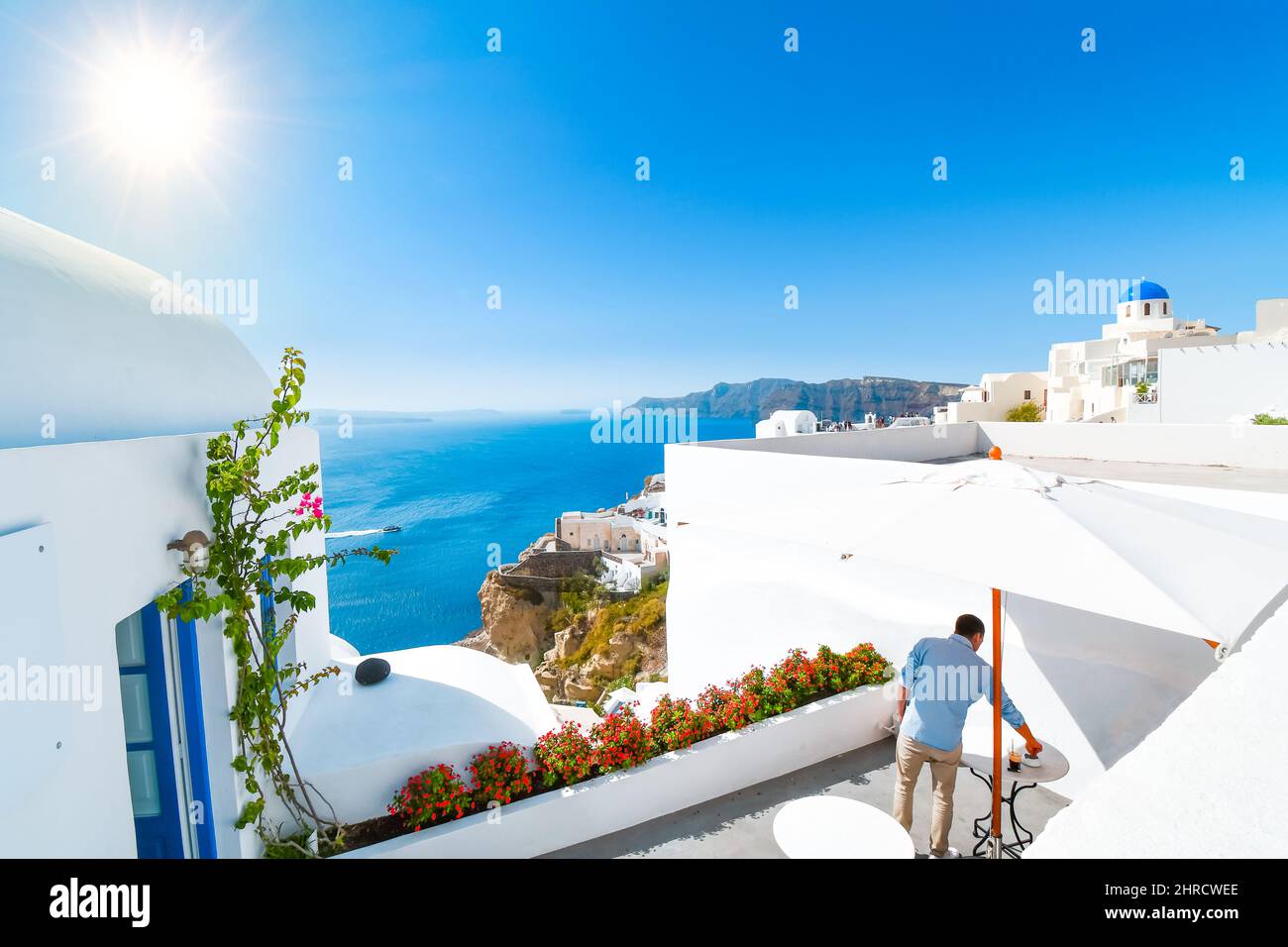 Un jeune homme adulte se détend sur la terrasse privée d'un complexe blanchi à la chaux sur l'île de Santorini, en Grèce, avec vue sur la mer et la ville. Banque D'Images