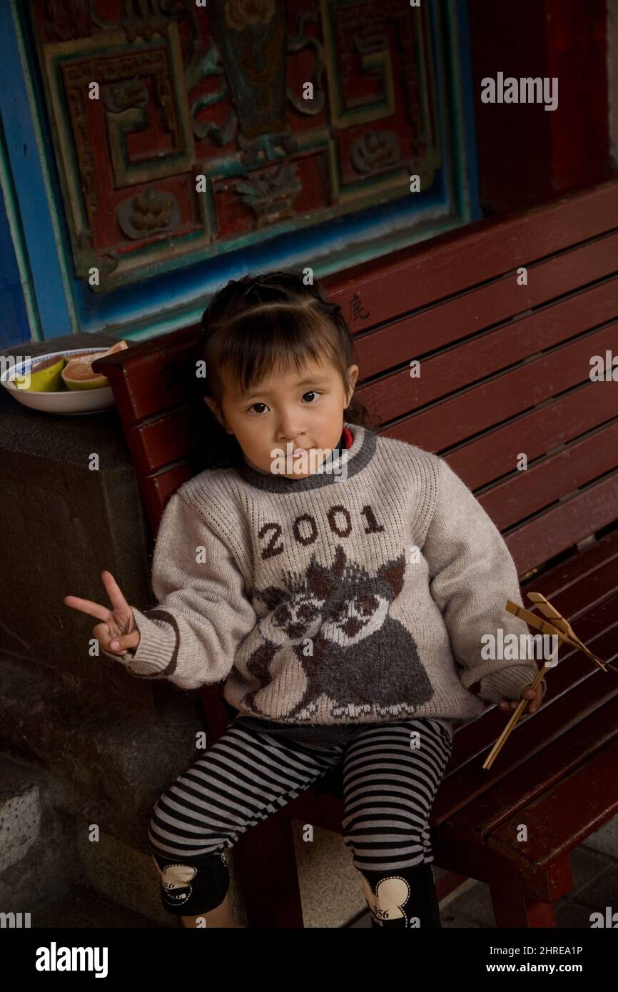 Une jeune fille pré-K sérieuse dans un chandail main-me-vers le bas 2001 donne le signe de paix devant sa maison dans la vieille ville de Lukang, le comté de Changhua, Taiwan Banque D'Images