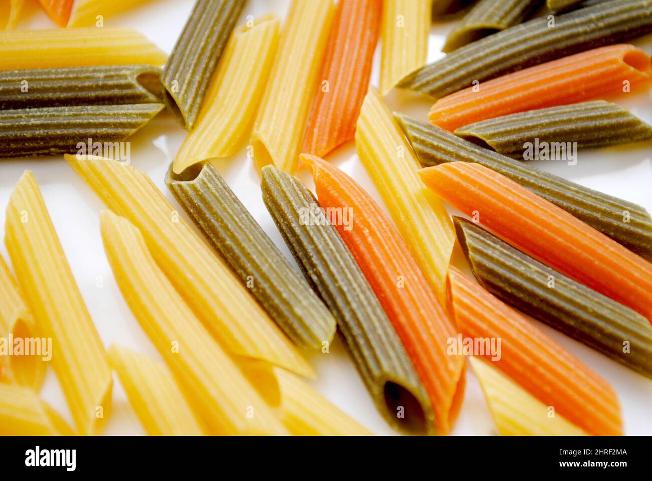 Gros plan de nouilles de pâtes Penne en forme de cylindre crues en trois couleurs jaune, vert et rouge Banque D'Images