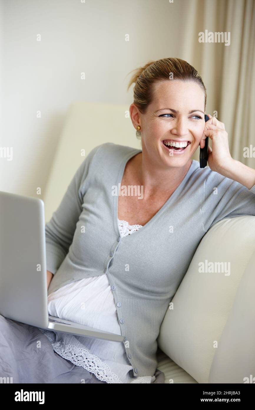 C'est génial de travailler de chez soi. Une jeune femme heureuse parlant sur son téléphone portable tout en étant assise avec son ordinateur portable. Banque D'Images