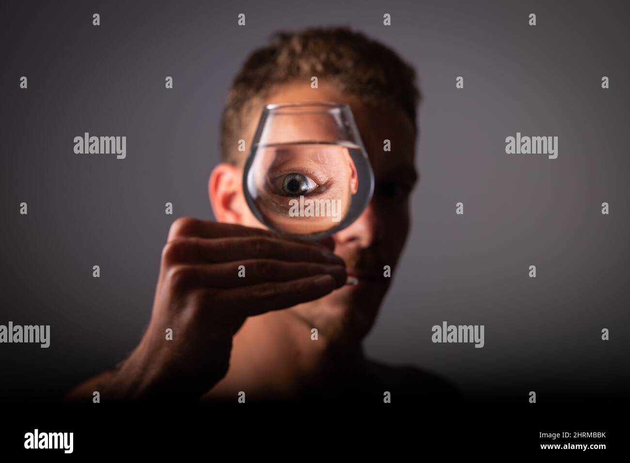 Gros plan de l'œil d'un garçon réfléchi dans un verre d'eau. Personne abstraite. Banque D'Images