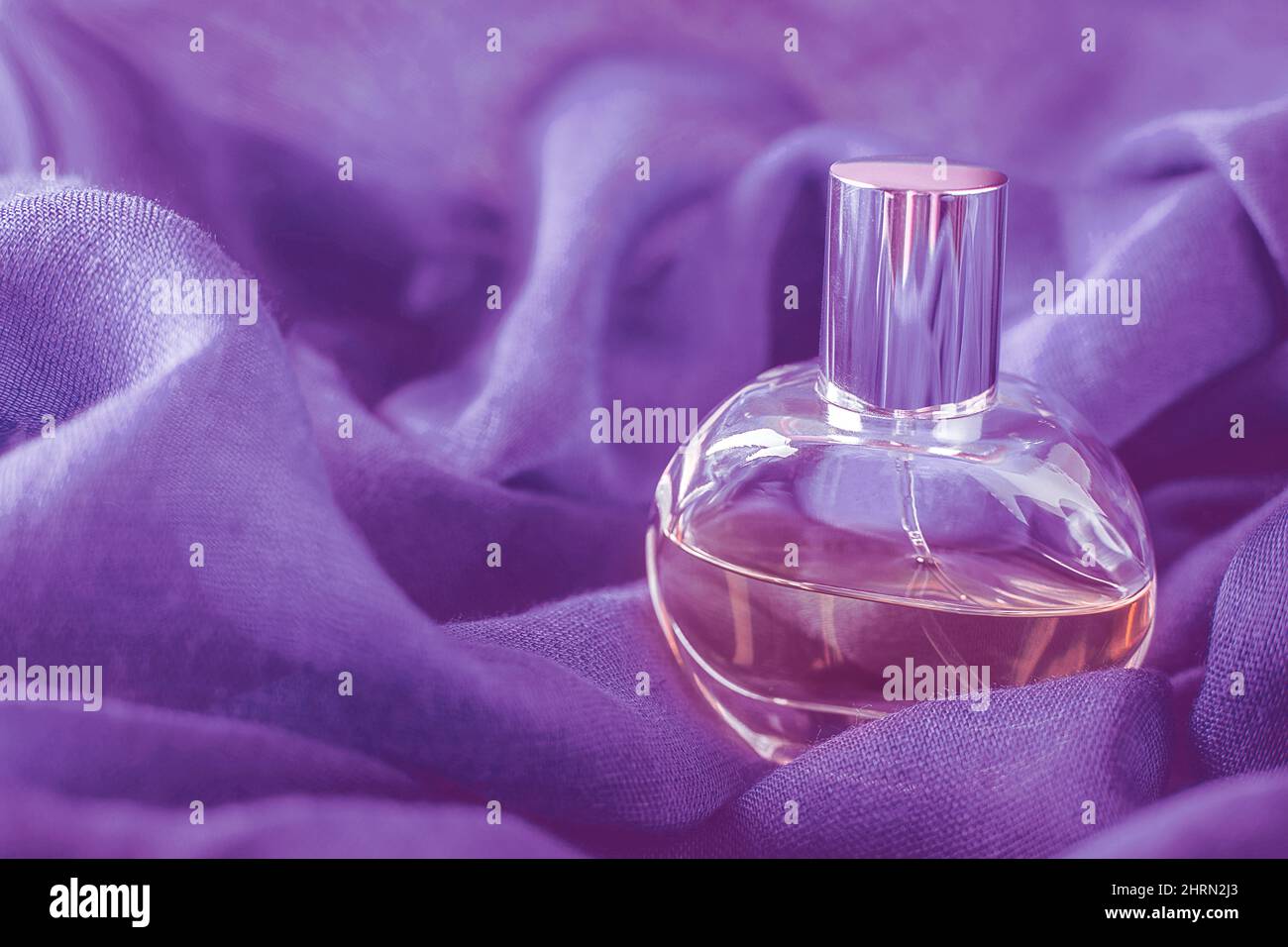 Bouteille en verre avec parfum sur fond de tissu très violet de péri. Gros plan avec espace de copie, mise au point souple. Banque D'Images