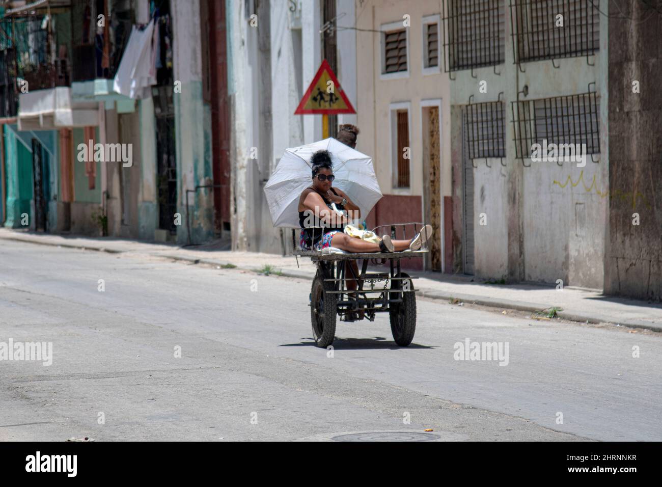 Une femme se déplace à l'arrière d'un vélo le long d'une rue à la Havane, Cuba comme un homme la conduit à travers un quartier. Banque D'Images