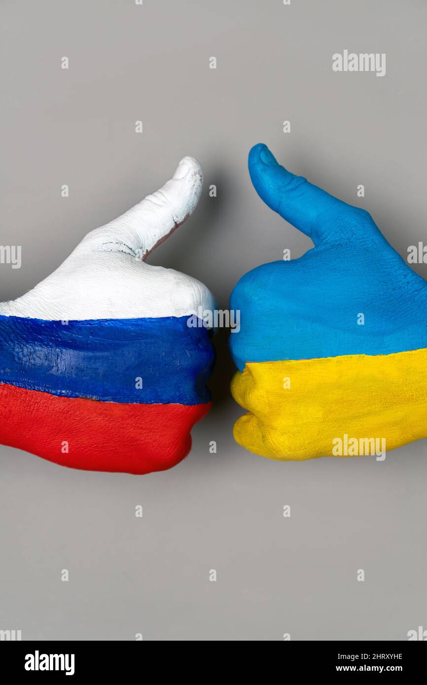 Les mains peintes dans les drapeaux de l'Ukraine et de la Russie soulèvent un doigt sur un fond gris. Vertical. Pouce vers le haut de la main avec le dessin d'un drapeau Banque D'Images