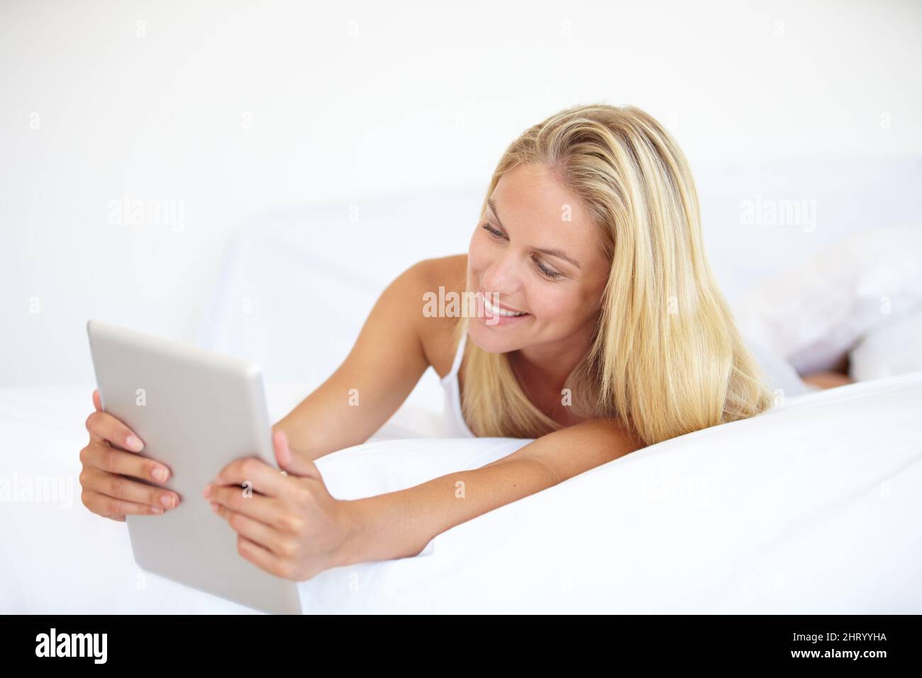 Navigation en toute confort. Une belle jeune femme blonde travaillant sur son pavé numérique tout en étant couché dans le lit. Banque D'Images