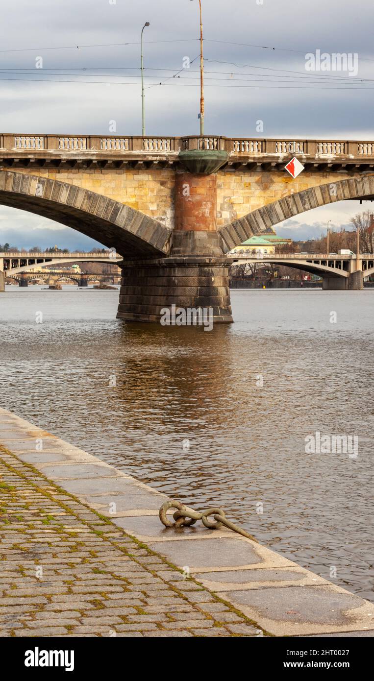 Un vieux anneau d'amarrage est fixé sur le quai en pierre de la Vltava. La pile du pont de pierre est jaune et les deux arches commencent de chaque côté. Banque D'Images