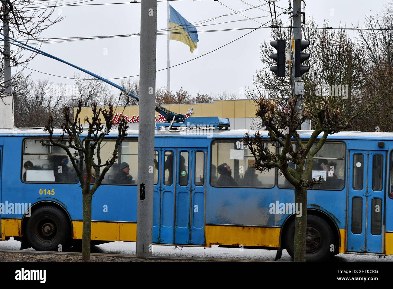 Les gens sont vus dans le trolley-bus peint dans les couleurs ukrainiennes et le drapeau national oukrianien sur le mât à Kramatorsk. Le président russe Vladimir Poutine a ordonné l'intervention militaire le 24 février, quelques jours après avoir reconnu deux enclaves séparatistes dans l'est de l'Ukraine. Il a affirmé que Moscou n'avait aucun plan pour occuper le pays voisin mais voulait "démilitariser" et "dénaziser" l'Ukraine. Le président ukrainien Volodymyr Zelenskyy a accusé la Russie d'essayer d'installer un gouvernement fantoche et a déclaré que les Ukrainiens défendront leur pays contre l'agression russe. Banque D'Images