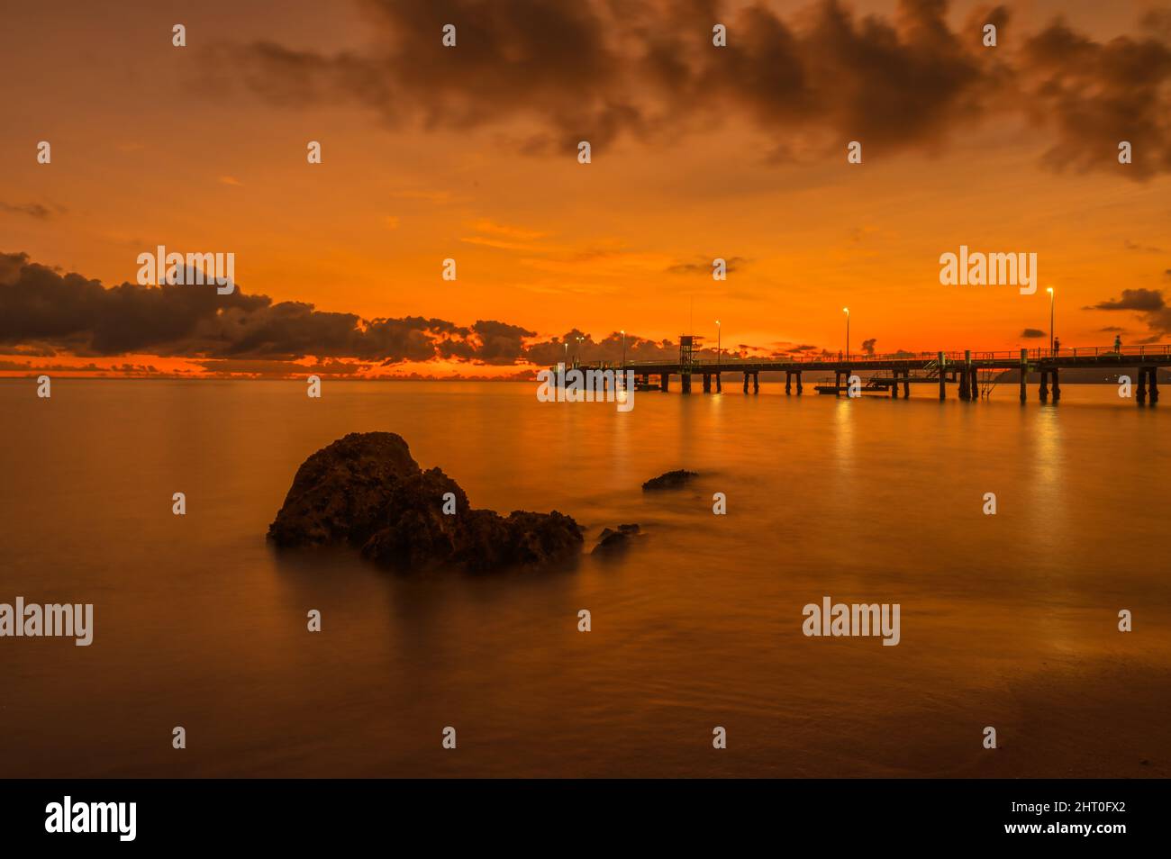 Un lever de soleil spectaculaire, vibrant, rouge/orange au-dessus de Palm Cove, avec des rochers en avant-plan incrustés d'huîtres, qui suscitent l'intérêt de l'emblématique jetée de QLD, en Australie. Banque D'Images