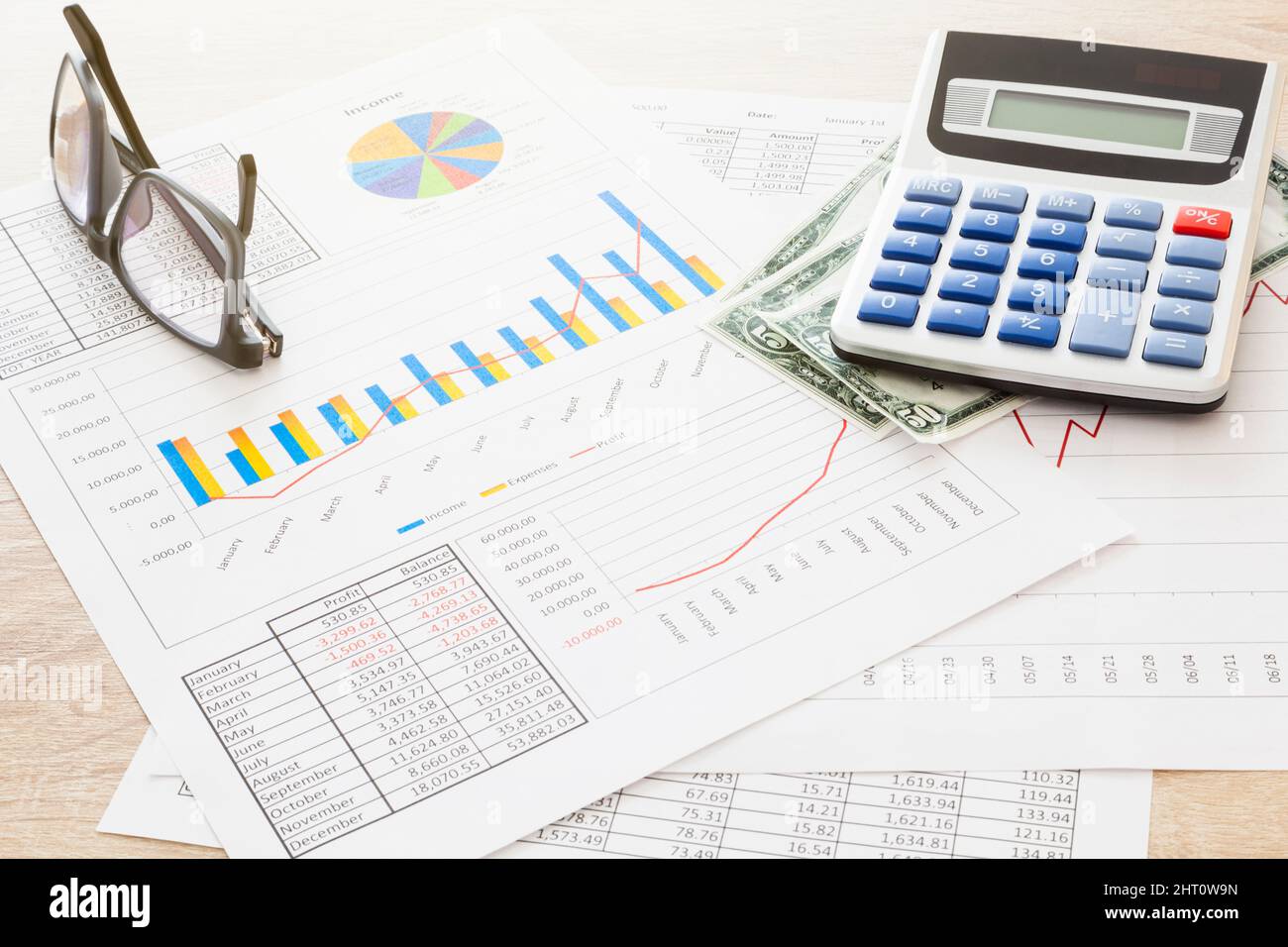 Sur un tableau se trouvent plusieurs feuilles de données et de graphiques économiques, des billets de banque, une paire de lunettes et une calculatrice électronique. Banque D'Images