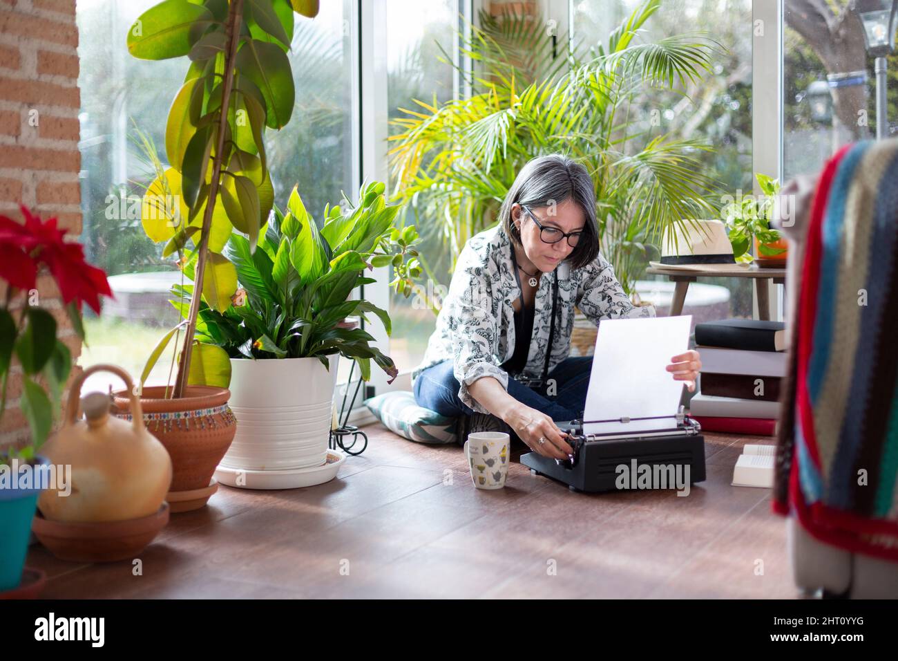 Femme adulte écrivaine mettant une feuille de papier vierge sur machine à écrire. Elle est à la maison. Banque D'Images