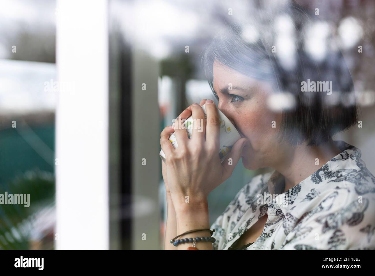 Gros plan sur une femme adulte qui boit du café. Elle est à la maison regardant dehors par la fenêtre. Banque D'Images