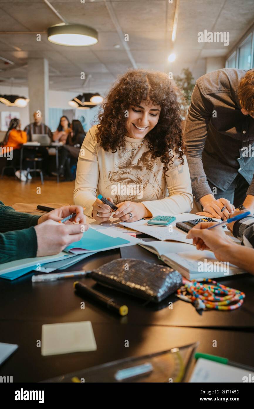 Femme souriante aux cheveux bouclés étudiant avec des amis à la cafétéria Banque D'Images