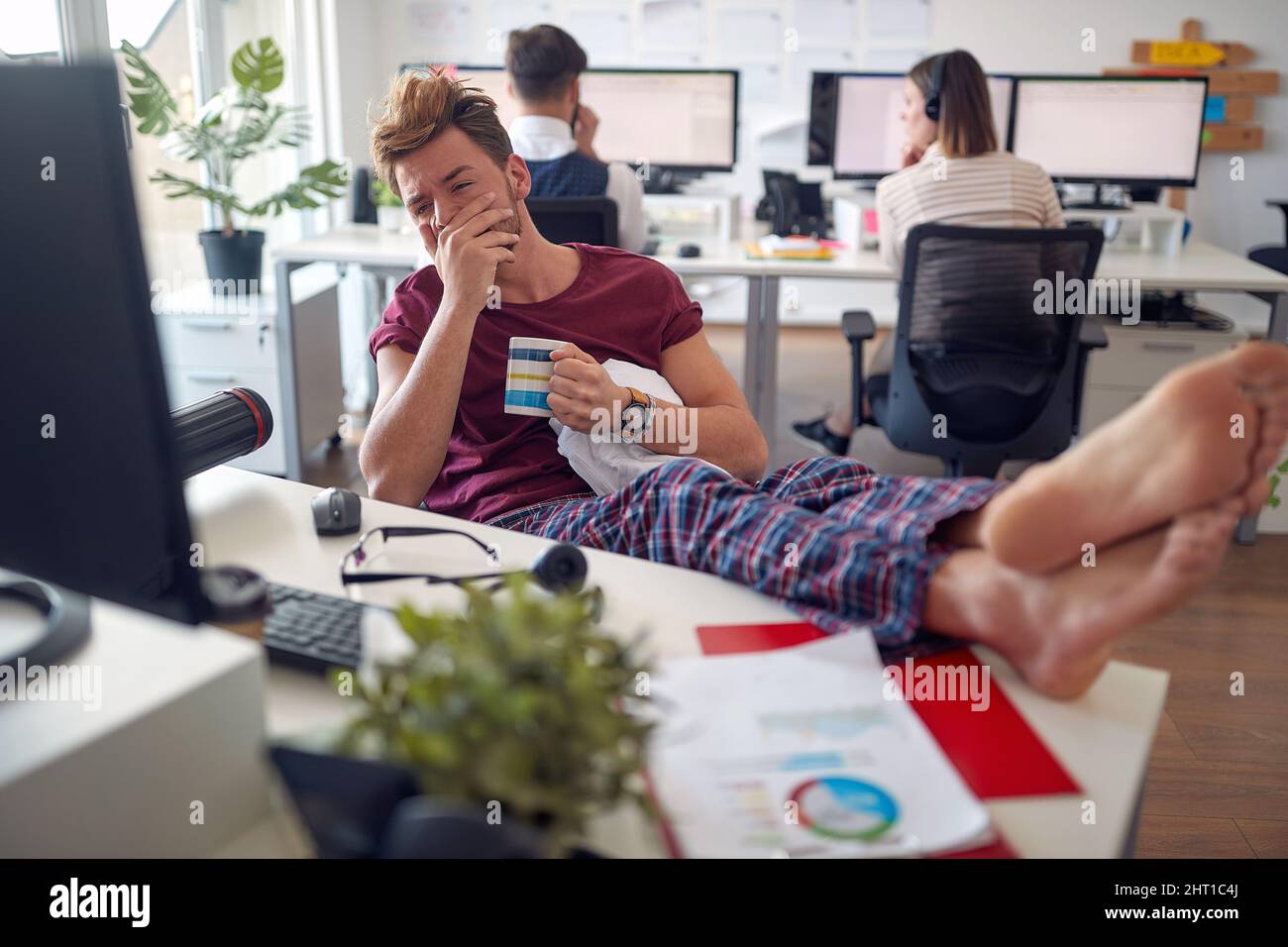 Un jeune homme travaille à la réception tout en étant assis de manière détendue dans une atmosphère agréable au bureau. Employés, travail, bureau Banque D'Images