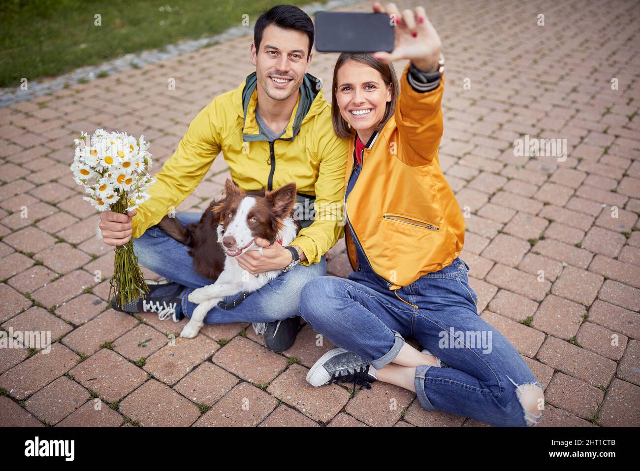 magnifique jeune femme en tenue décontractée avec un jean déchiré sur son genou prenant le selfie d'elle-même et un petit ami assis avec les jambes croisées et un chien dans t Banque D'Images