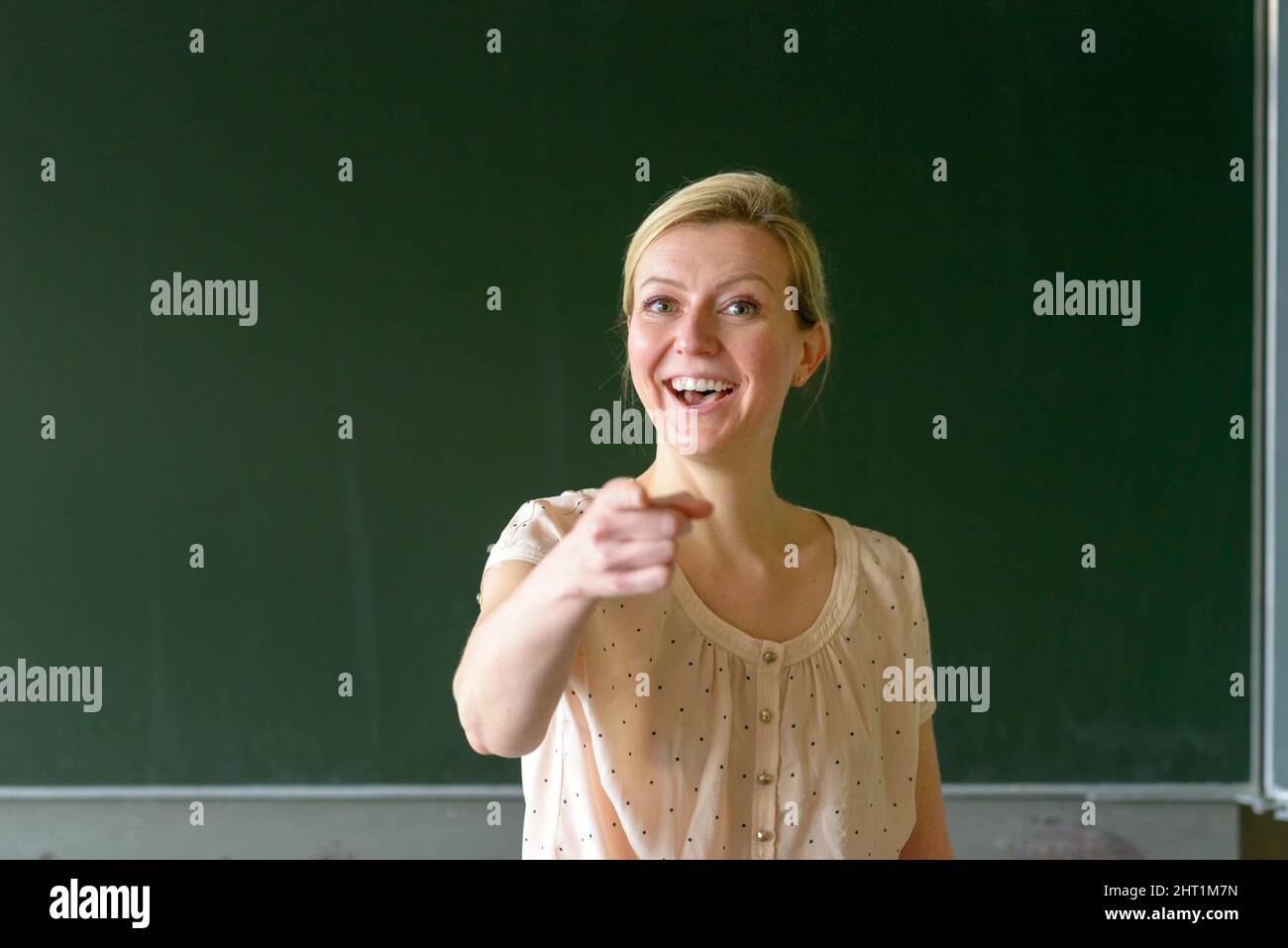 Professeur d'école debout devant un tableau noir dans la salle de classe pointant avec son doigt vous disant Banque D'Images