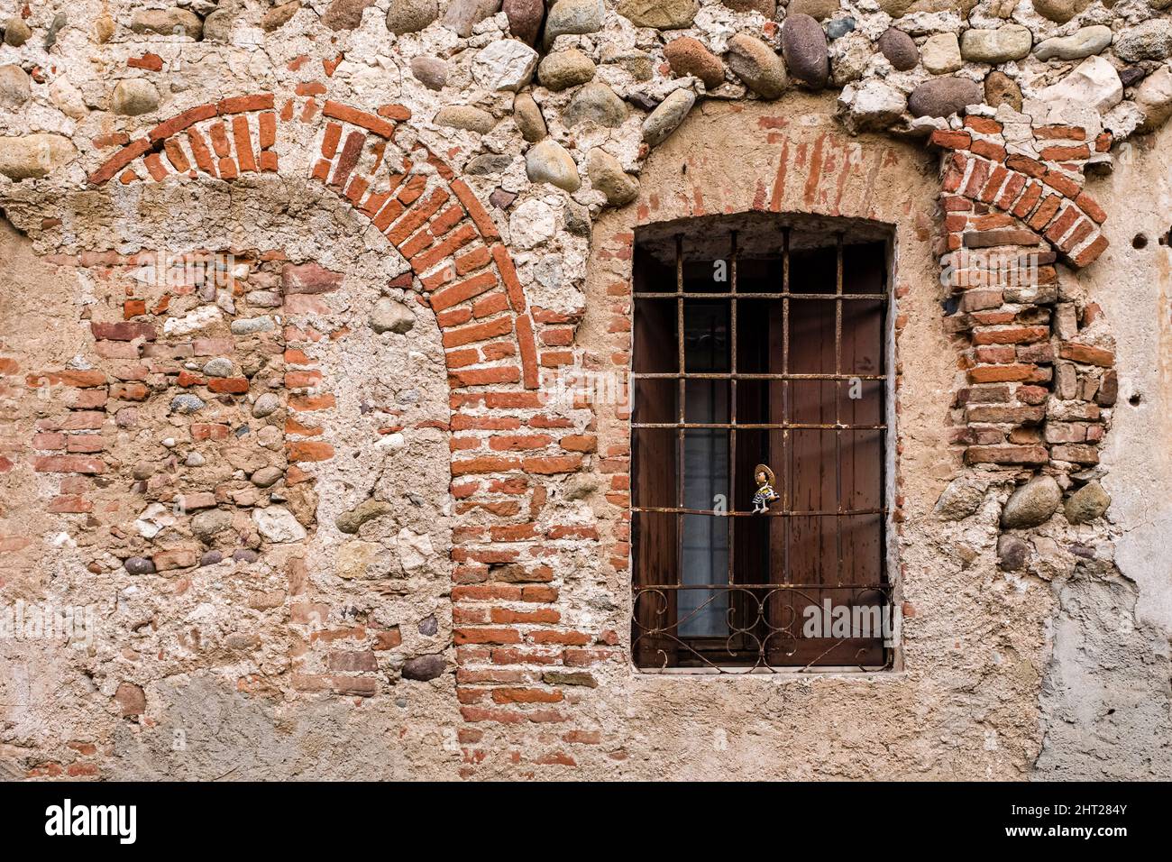 Façade rocheuse d'une maison médiévale de Bassano del Grappa avec une fenêtre barrée, une petite poupée placée dans la fenêtre. Banque D'Images