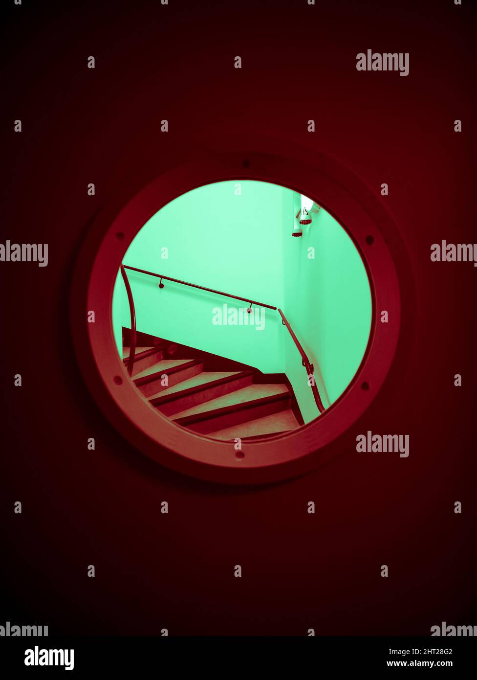 Plan vertical de l'escalier rouge avec des murs vert clair à travers un hublot de porte rouge Banque D'Images