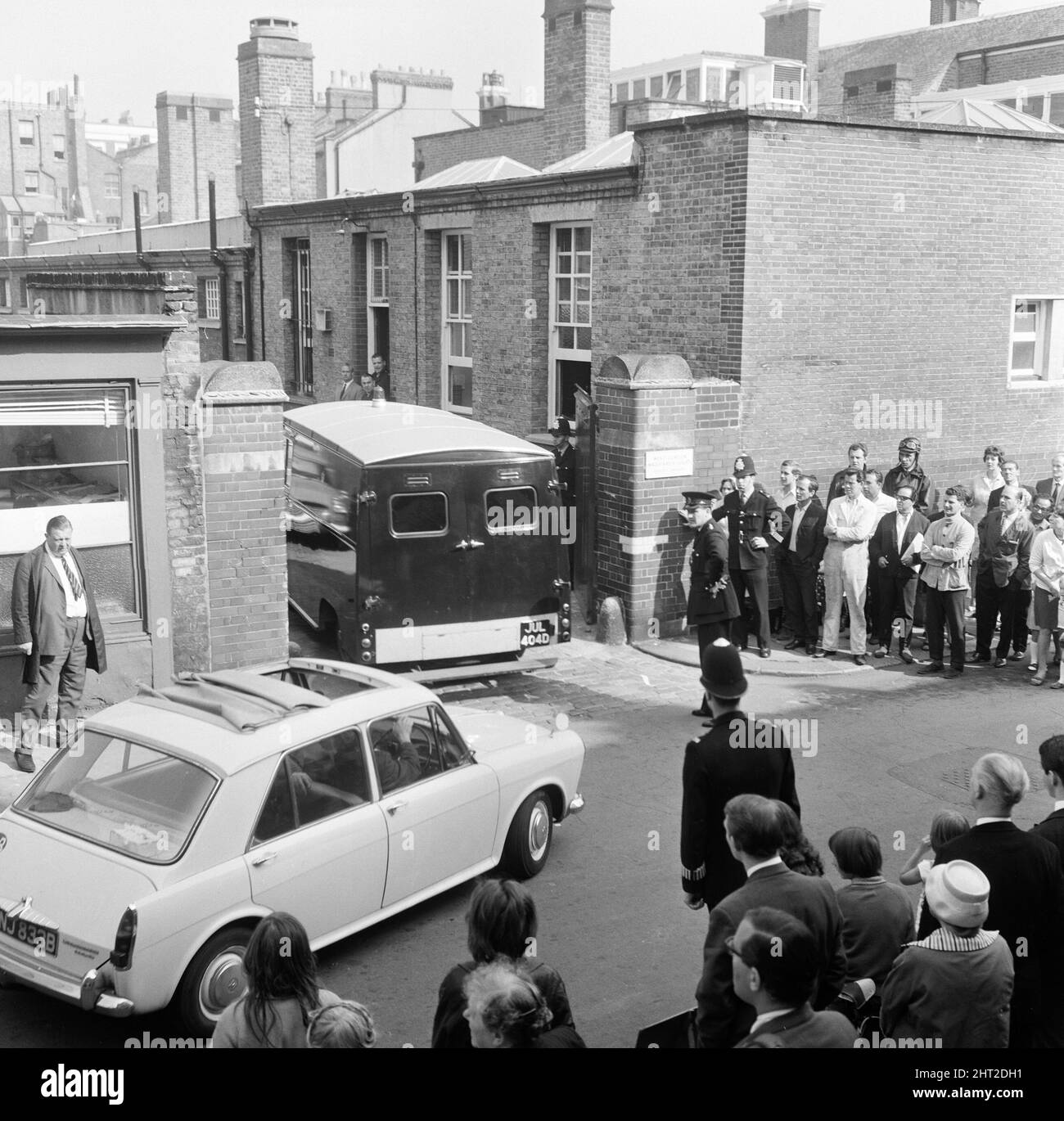John Edward Witney, 36 ans, qui a été accusé du meurtre de 3 policiers, a été emmené du poste de police de Shepherds Bush (le QG du meurtre) et conduit au tribunal de la magistrature de West London, où il a fait une brève comparution et a été remis en détention jusqu'en août 23. La camionnette de police contenant Witney arrive au West London court, suivie d'une voiture de police. 16th août 1966. Banque D'Images