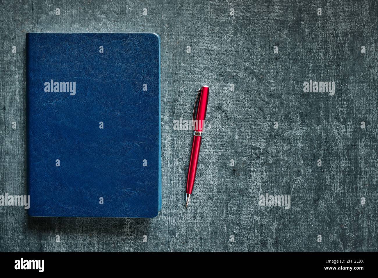 Agenda d'affaires en cuir bleu et stylo à bille rouge sur table de bureau grise Banque D'Images