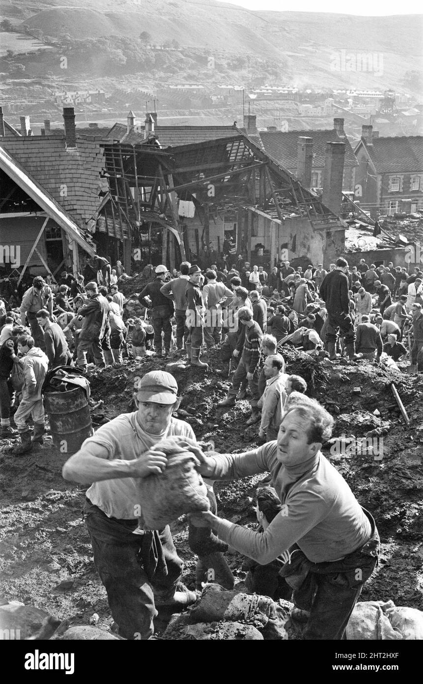 Aberfan - 21st octobre 1966 les hommes locaux et les services d'urgence creusent à la hâte dans la boue pour les survivants de la Pantans Junior School. Ils forment des lignes pour déplacer des seaux de boue, d'un à l'autre, loin de la scène. Et pour être en ligne, en se déplaçant vers le haut de la file d'attente pour leur tour à creuser. Deux hommes vus avec un sac de sable rempli, plein de boue, qui a été utilisé pour faire un mur en cas de glissement de terrain ultérieur. Le désastre d'Aberfan a été l'effondrement catastrophique d'un pourboire de collierie dans le village gallois d'Aberfan, près de Merthyr Tydfil. Il a été causé par une accumulation d'eau dans le rocher accumulé et le schiste, Banque D'Images