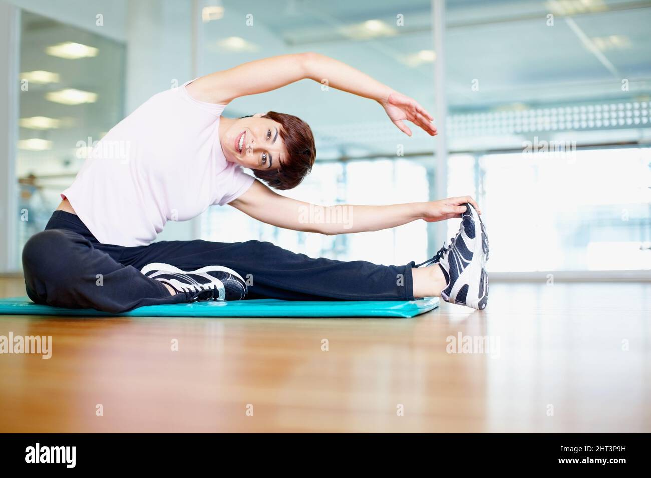 Femme étirant. Portrait d'une femme souriante faisant un exercice d'étirement en salle de gym. Banque D'Images