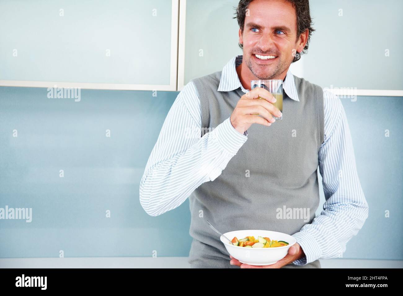 Homme mûr souriant avec hors-d'œuvre et salade de fruits. Homme mûr souriant qui regarde loin avec du jus de citron et de la salade de fruits. Banque D'Images
