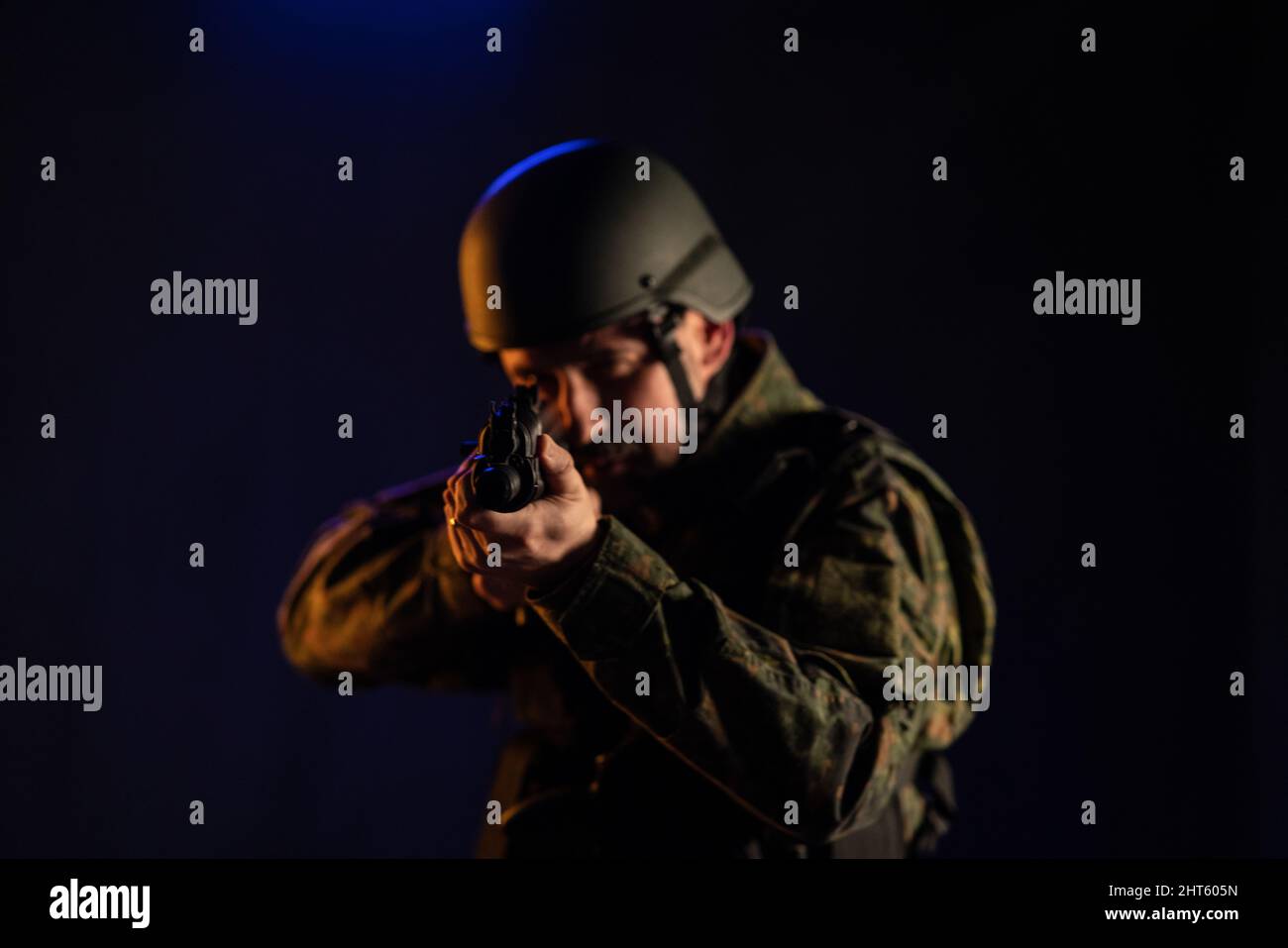 Soldat en uniforme militaire et casque visant de l'arme à la caméra sur fond noir. Banque D'Images