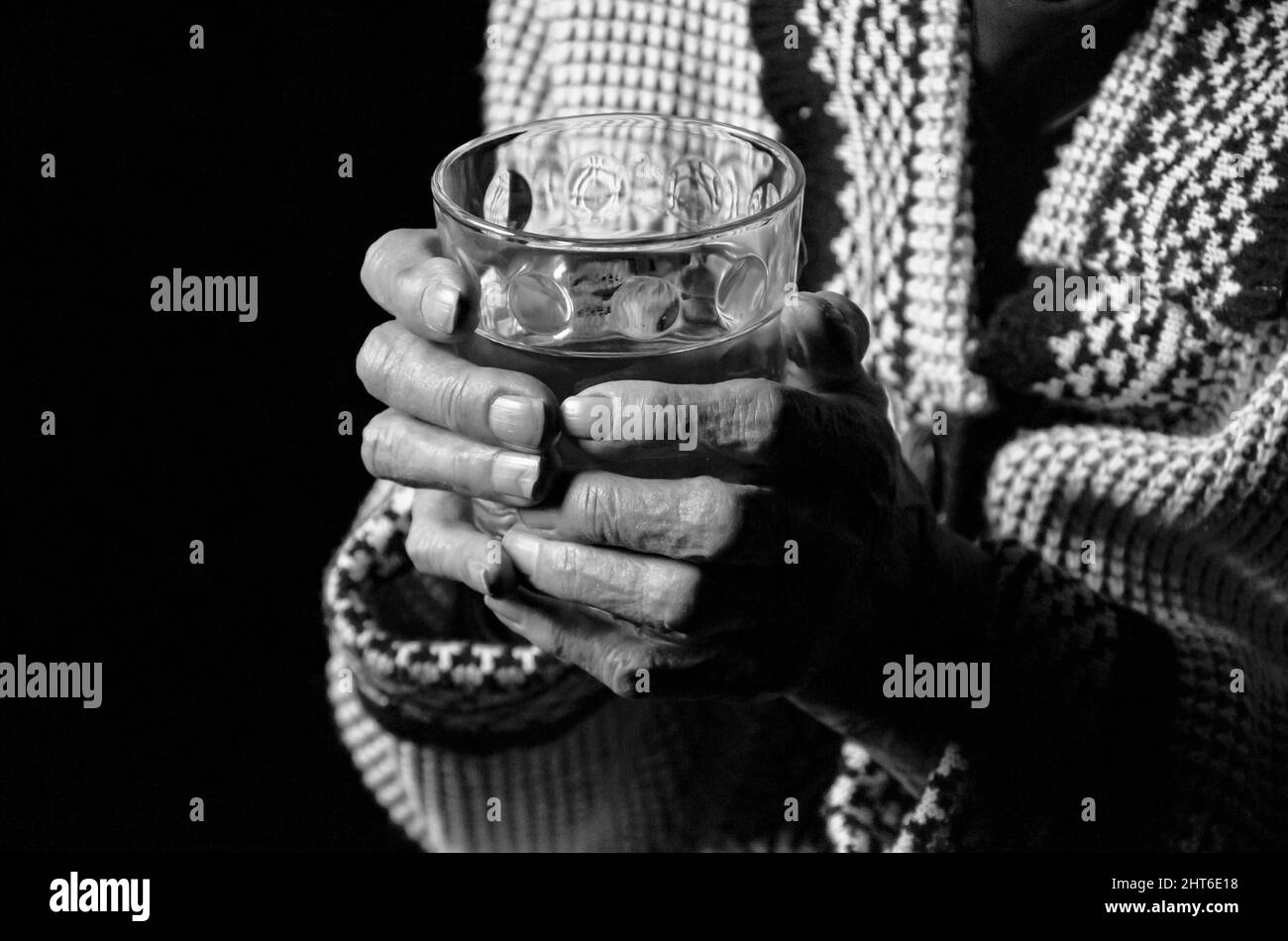Portrait d'une femme âgée avec un verre d'eau sur fond noir. Photo en noir et blanc. Banque D'Images